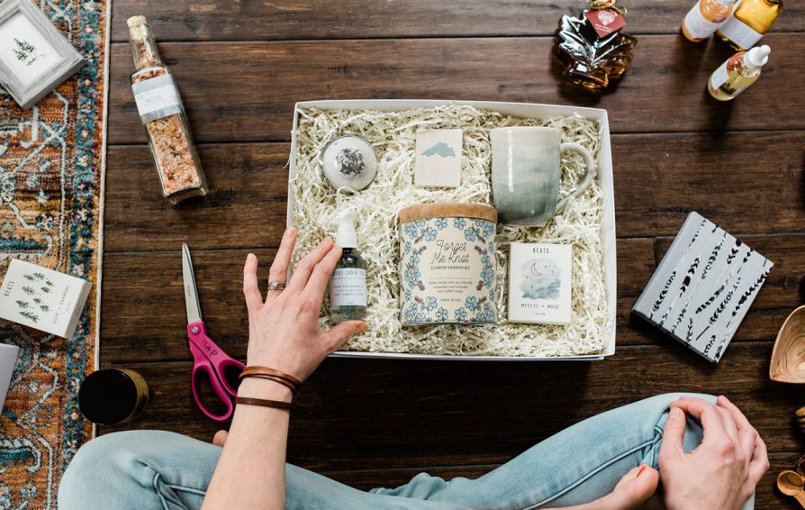 a person sitting cross legged on the floor in front of a gift box with various gifts inside