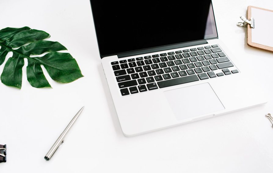 Home office workspace. Laptop with black screen, clipboard, palm leaf and accessories.