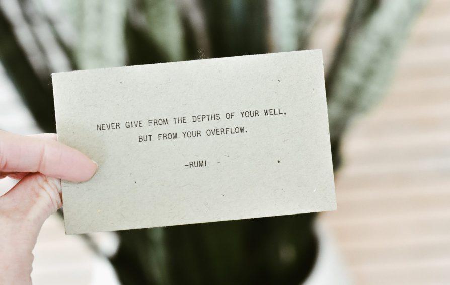 A hand holds a notecard stating a quote by Rumi.