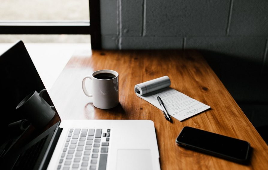 laptop on a wood desk with a notebook and coffee mug