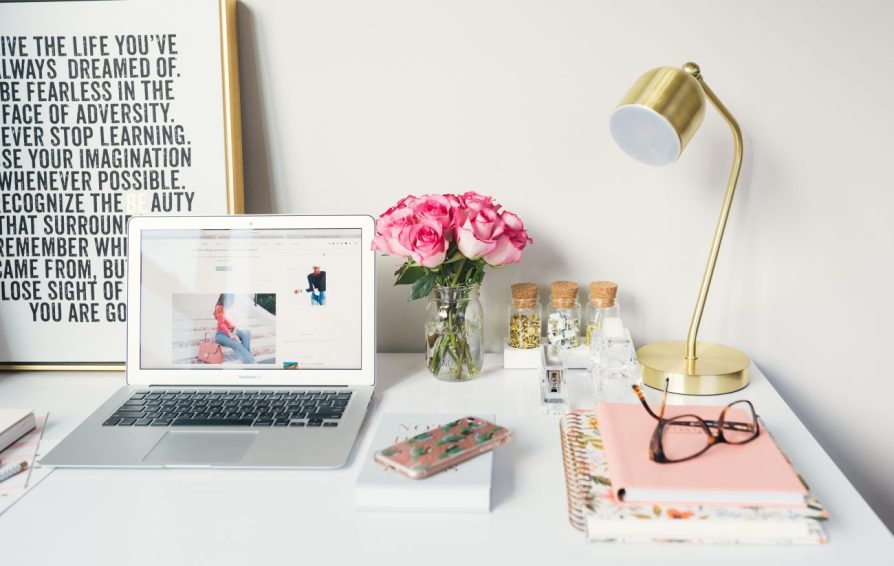 an open laptop on a desk decorated with flowers and a lamp