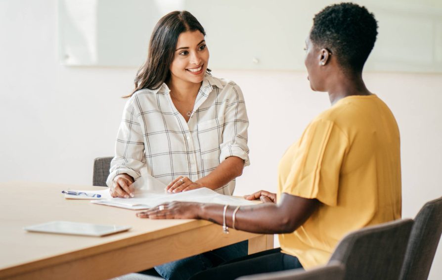 Woman business owner asking client background questions to another woman as they're seated