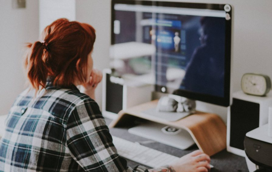 A woman with dark red hair sits facing a computer monitor where she's branding a website design