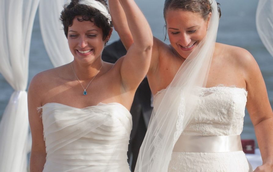 Newly wed brides lift their arms together in celebration