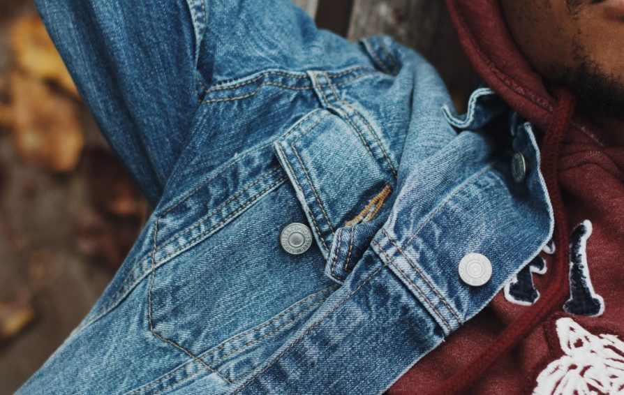 Close up of a man sleeping outdoors. He wears a maroon hoodie and denim jacket.