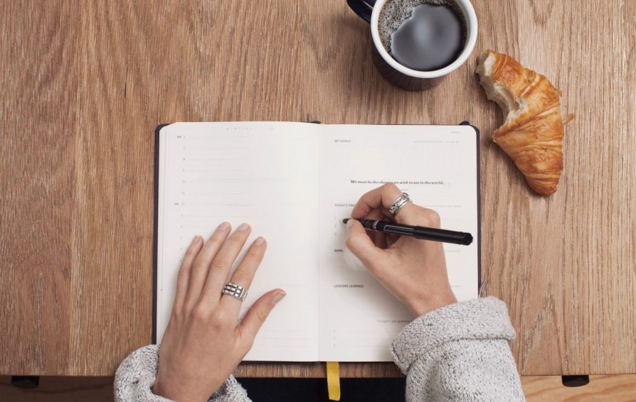 a woman writing goal setting questions in an open notebook on a wood desk