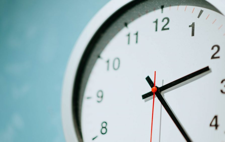 Close up of a white clock on a teal wall.