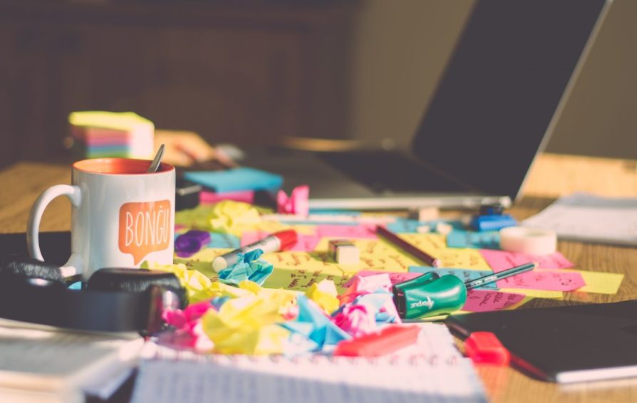Desk full of crumpled post-its, paper, and a coffee mug.