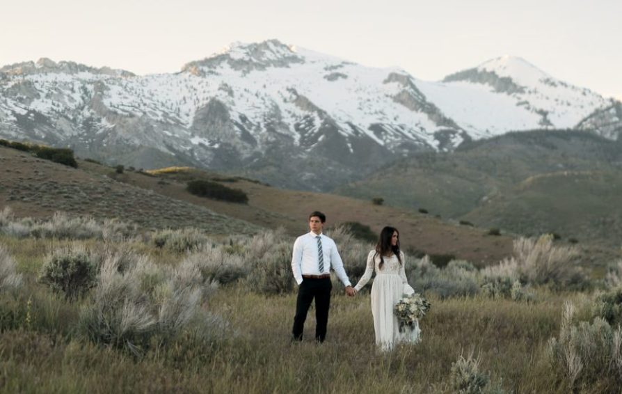 a bride and groom holding hands posing in front of a mountain
