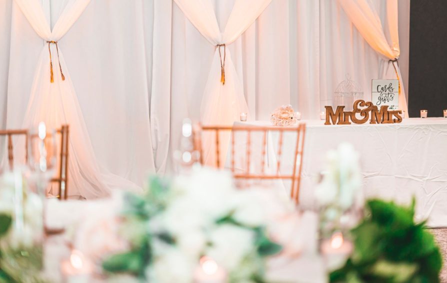 A wedding table with a Mr. & Mrs. sign sits in front of a wall of curtains with floral arrangements in the foreground