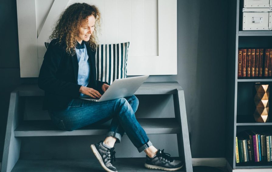Freelance businesswoman with notebook on her laps sitting on stairs and typing on keyboard.