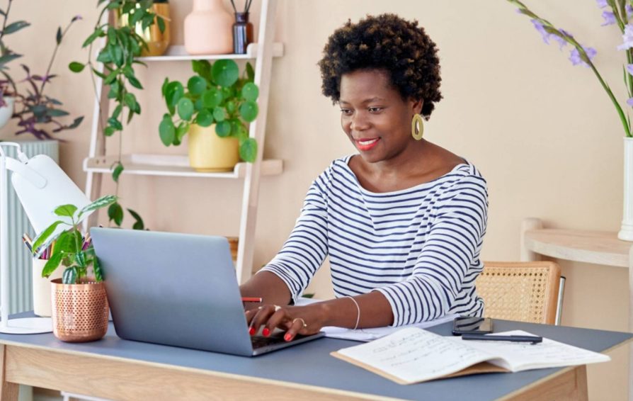A woman works at a desk in a room decorated with plants.