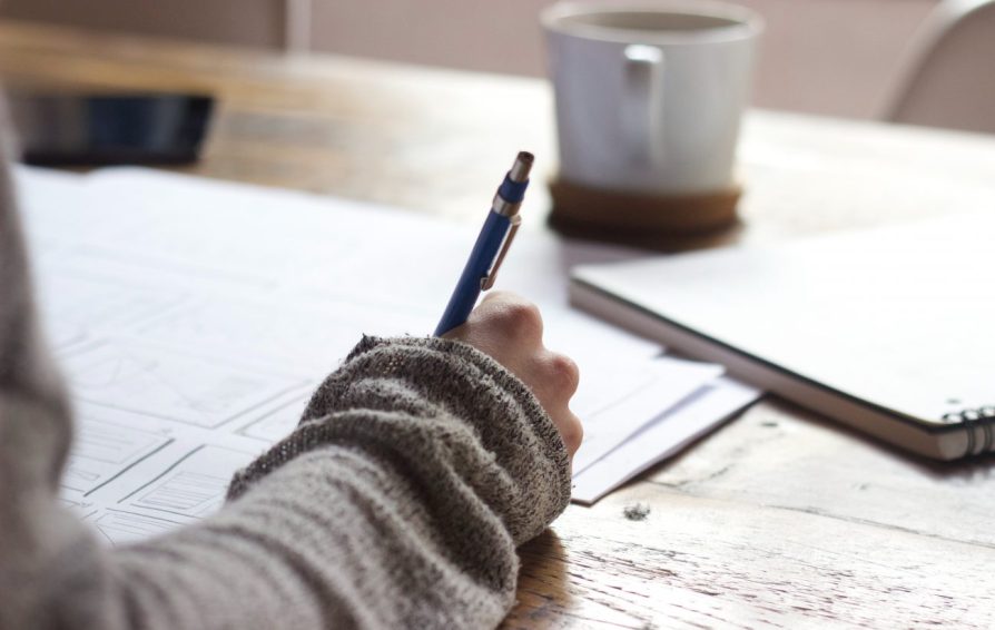a person writing at a desk with coffee in the background