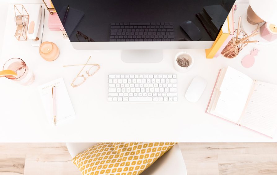 Aerial view of a white desk styled with assorted pink accessories and an iMac with keyboard.