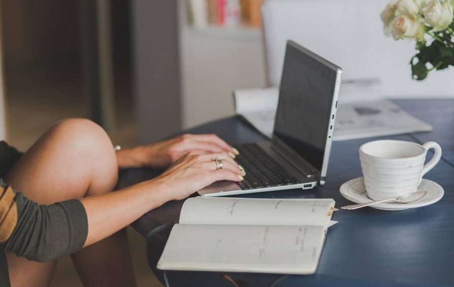 Person on laptop with notebook and coffee cup next to them