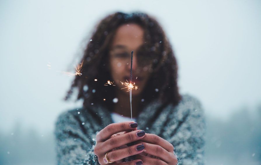 A woman holds a lit sparkler towards the camera.