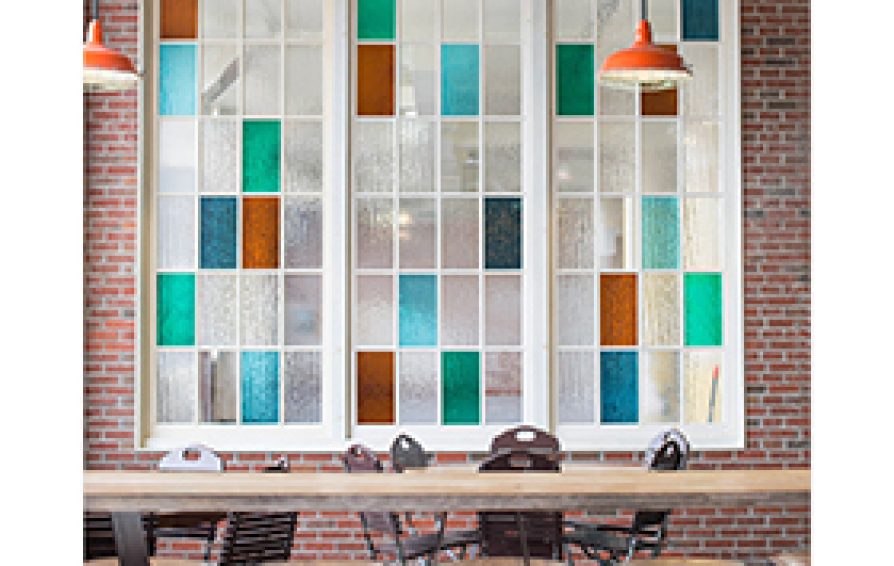 A long wooden table with chairs in front of a brick wall with a color-blocked glass window