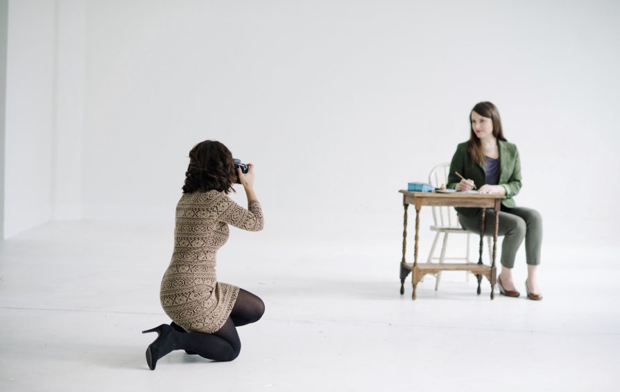 photographer taking a photo of a woman posed at a desk