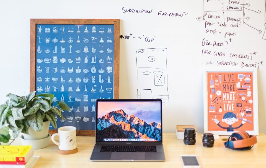 a desk scene with a laptop, coffee mug, poster and whiteboard