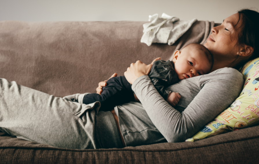 a mom laying on her back on a couch with her baby laying on her stomach
