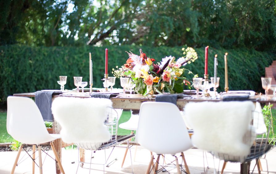 A dining table outside set with candles and a floral centerpiece.