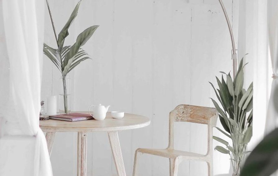 a white oak table with a chair and a silver floor lamp with plants