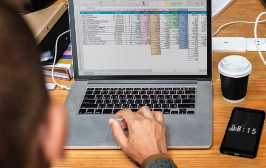 Over the shoulder image of a man typing out his business plan in a spreadsheet.