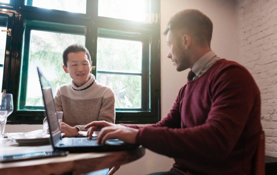 A man selling services to another man while at a table with a laptop