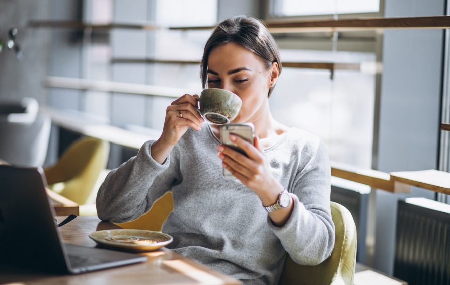 A woman drinks from a mug as she looks at her phone.