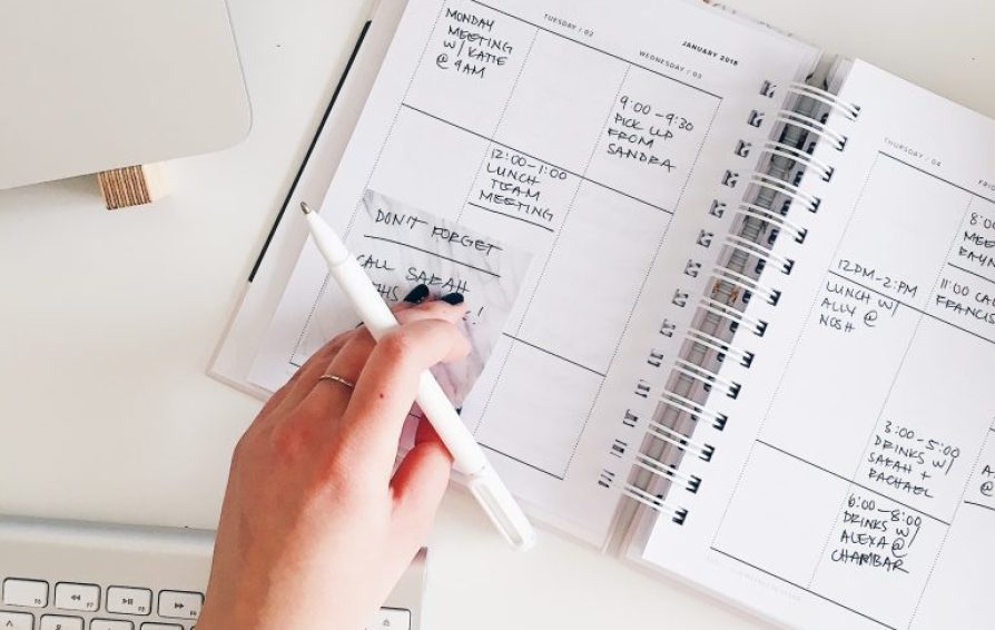 Top down view of a womans hand placing a post-it on a calendar.