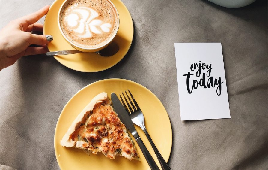 A hand places a latte next to a slice of savory pie and a note stating 