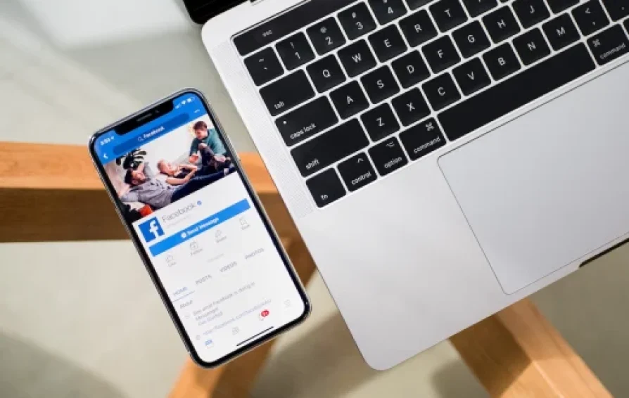 photographer on a phone next to a laptop with facebook ads