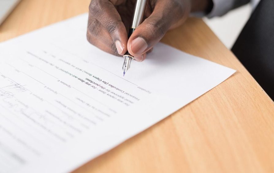 Close-up of a person signing a legal contract with a pen on a wooden desk