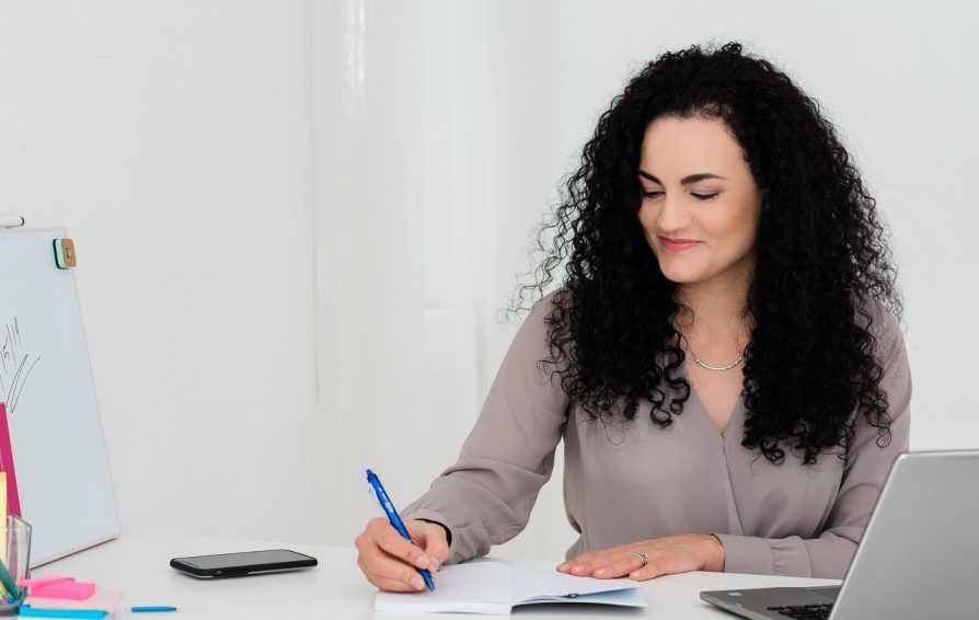 Woman working on client strategy as her desk, writing on a pad with a pen