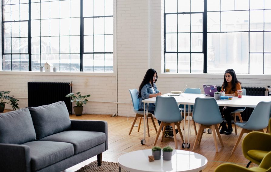 Two women work at a table in a large, loft space.
