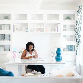 A woman in a stylish white office smiles down at her desk
