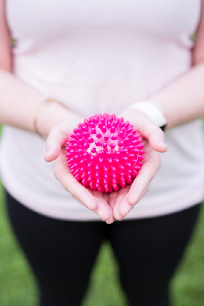 Close up of hands holding a spiky, pink yoga ball.