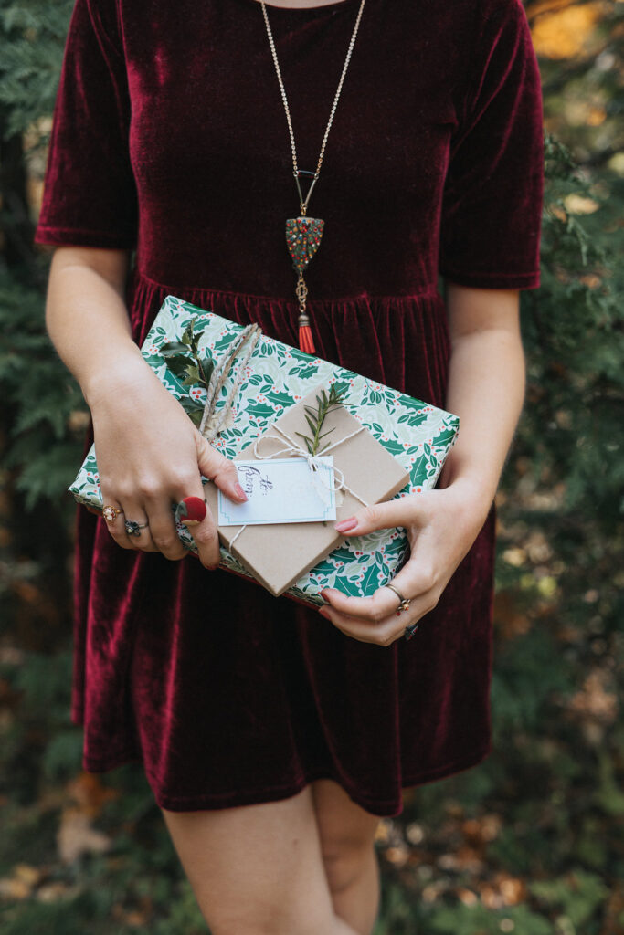 Close up of a stylishly wrapped gift, held by a woman wearing a burgundy velvet dress.