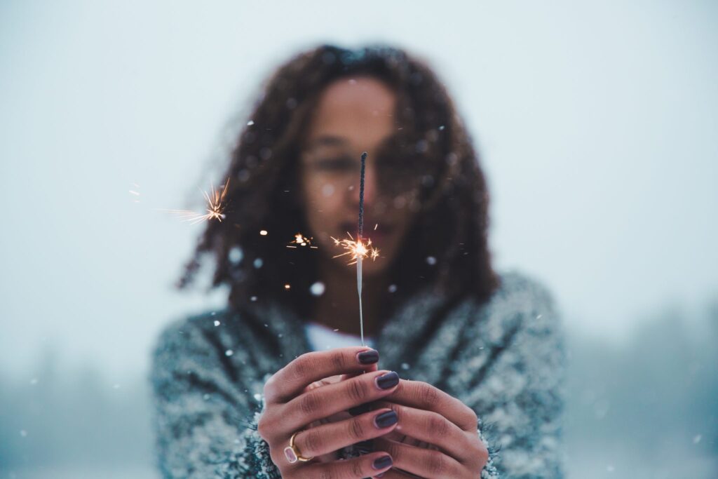 A woman holds a lit sparkler towards the camera.