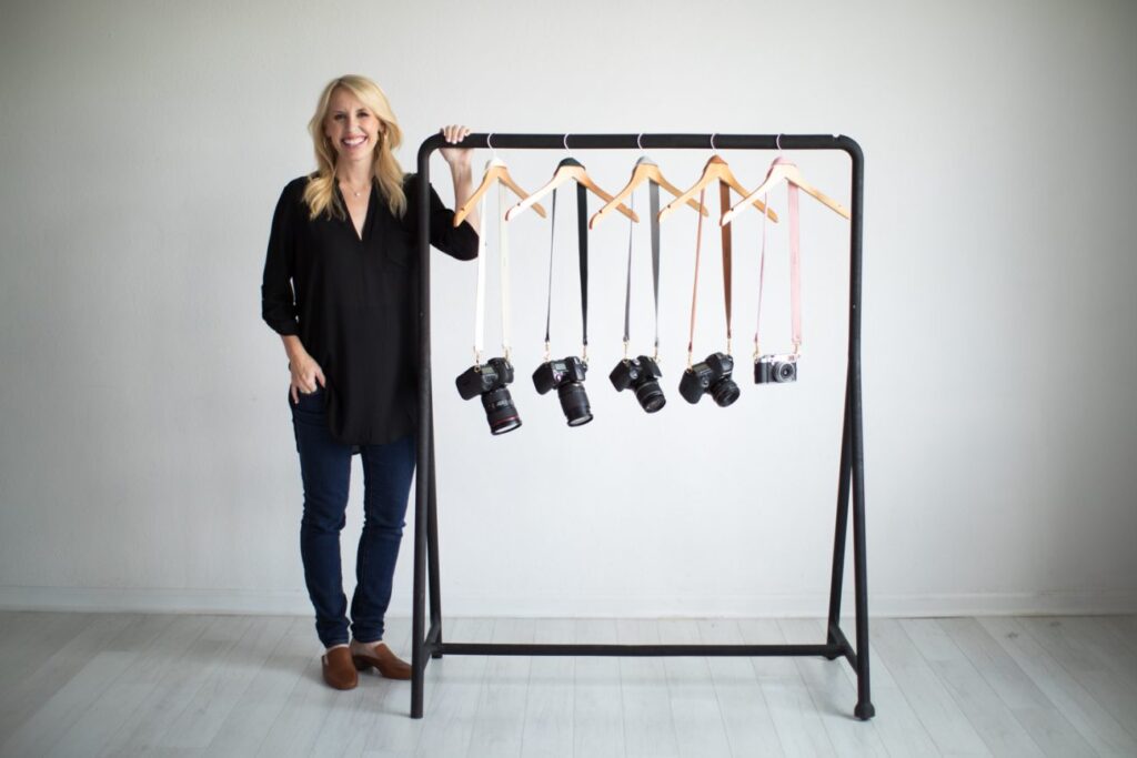woman dressed in black standing next to a clothes rack with cameras hanging on hangers