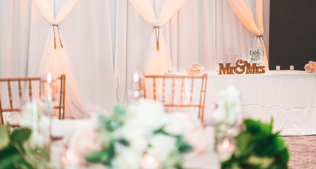 A wedding table with a Mr. & Mrs. sign sits in front of a wall of curtains with floral arrangements in the foreground