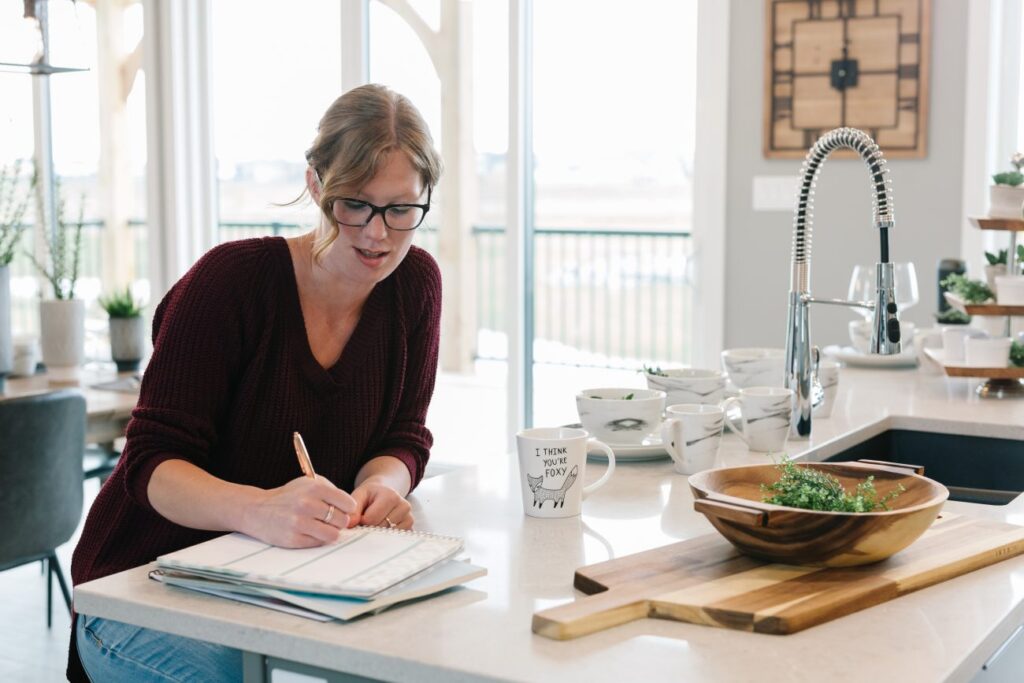 a woman sitting at her kitchen counter writing in a notebook