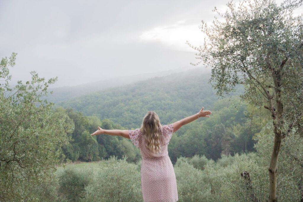 woman with her arms outstretched in front of a wooded hill
