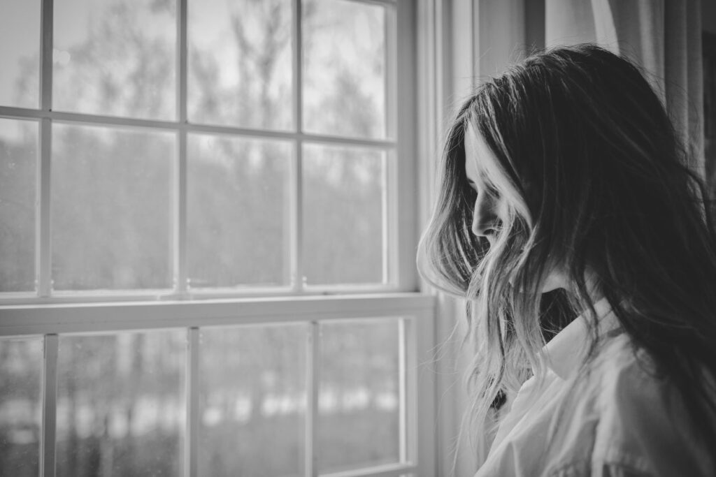 Black and White Image of Woman Looking Out Window
