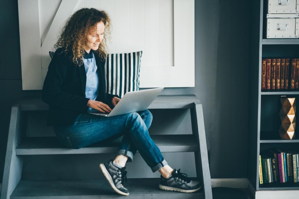 Freelance businesswoman with notebook on her laps sitting on stairs and typing on keyboard.