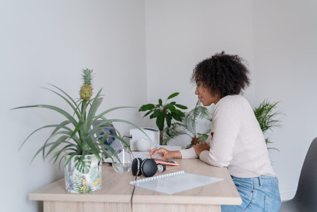 a woman sitting at a desk with plants tapping on her smartphone