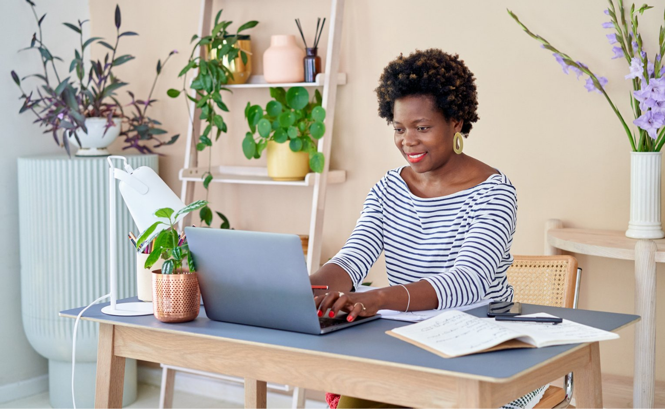 A black woman sits at a table while looking down at a table and smiling