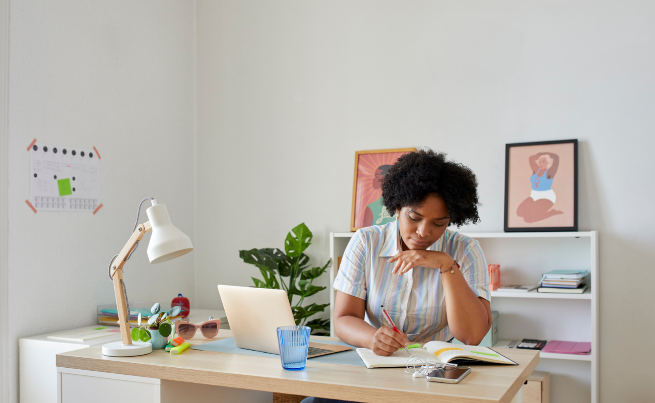 A woman at a desk looks down at a notepad where she's writing