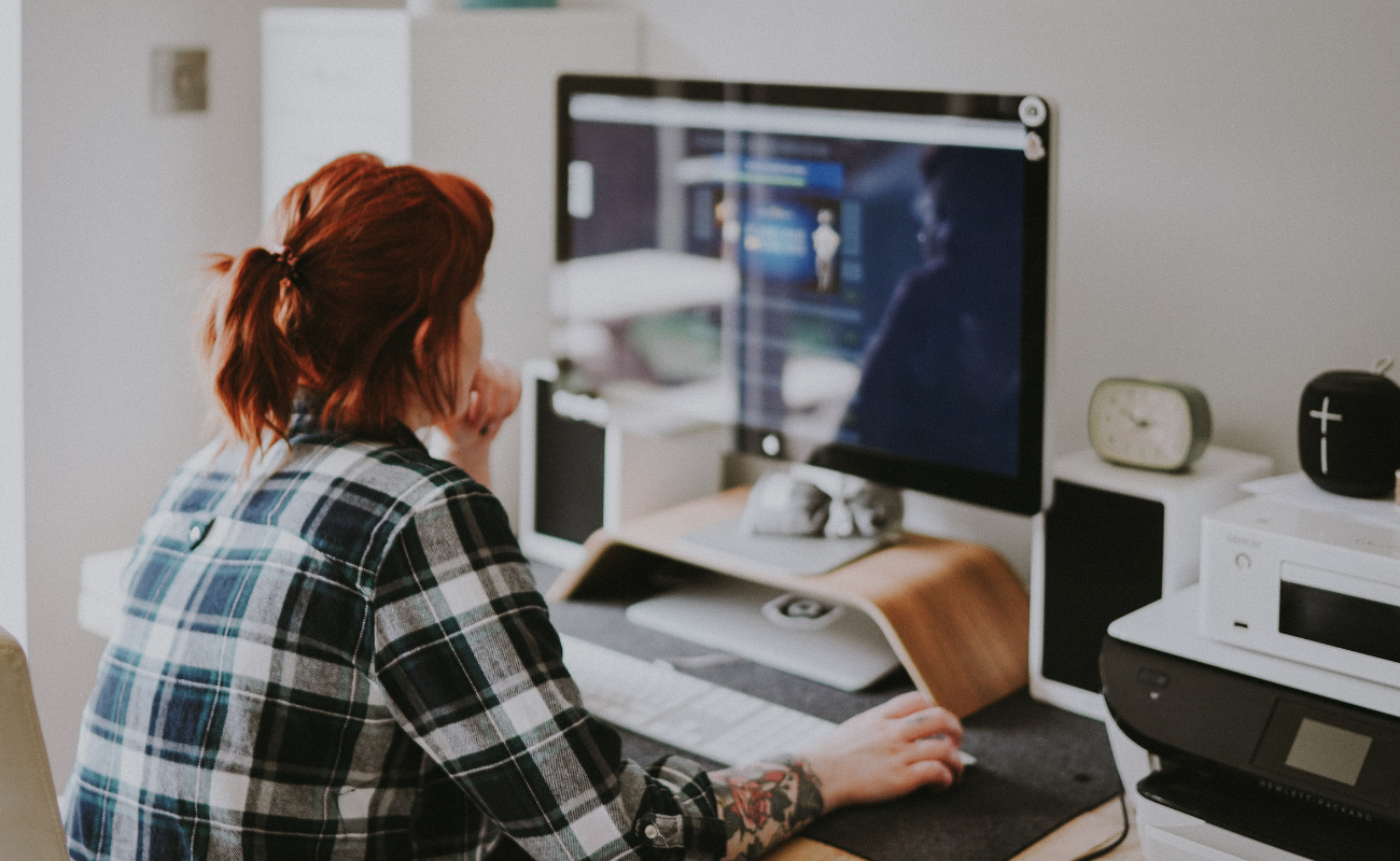 A woman with dark red hair sits facing a computer monitor where she's branding a website design