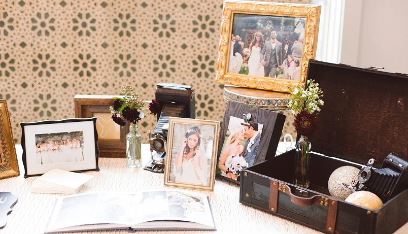 A table decorated with wedding photographs, old cameras, and a vintage suitcase.